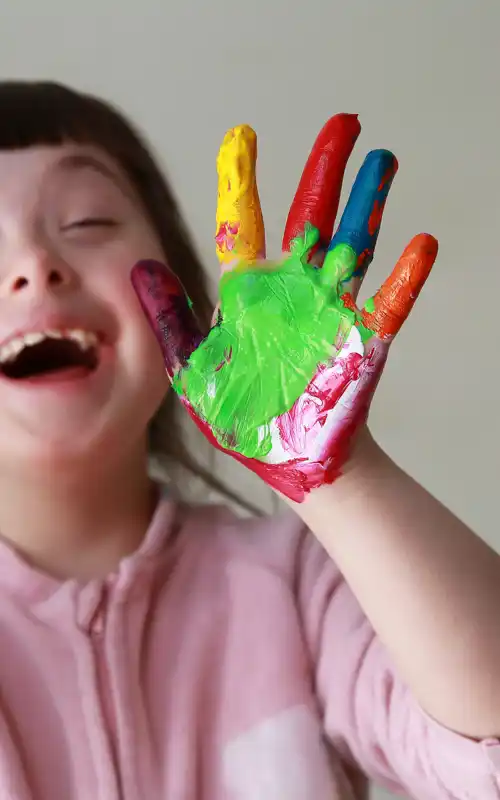A child with paint messily on her hands smiling and laughing