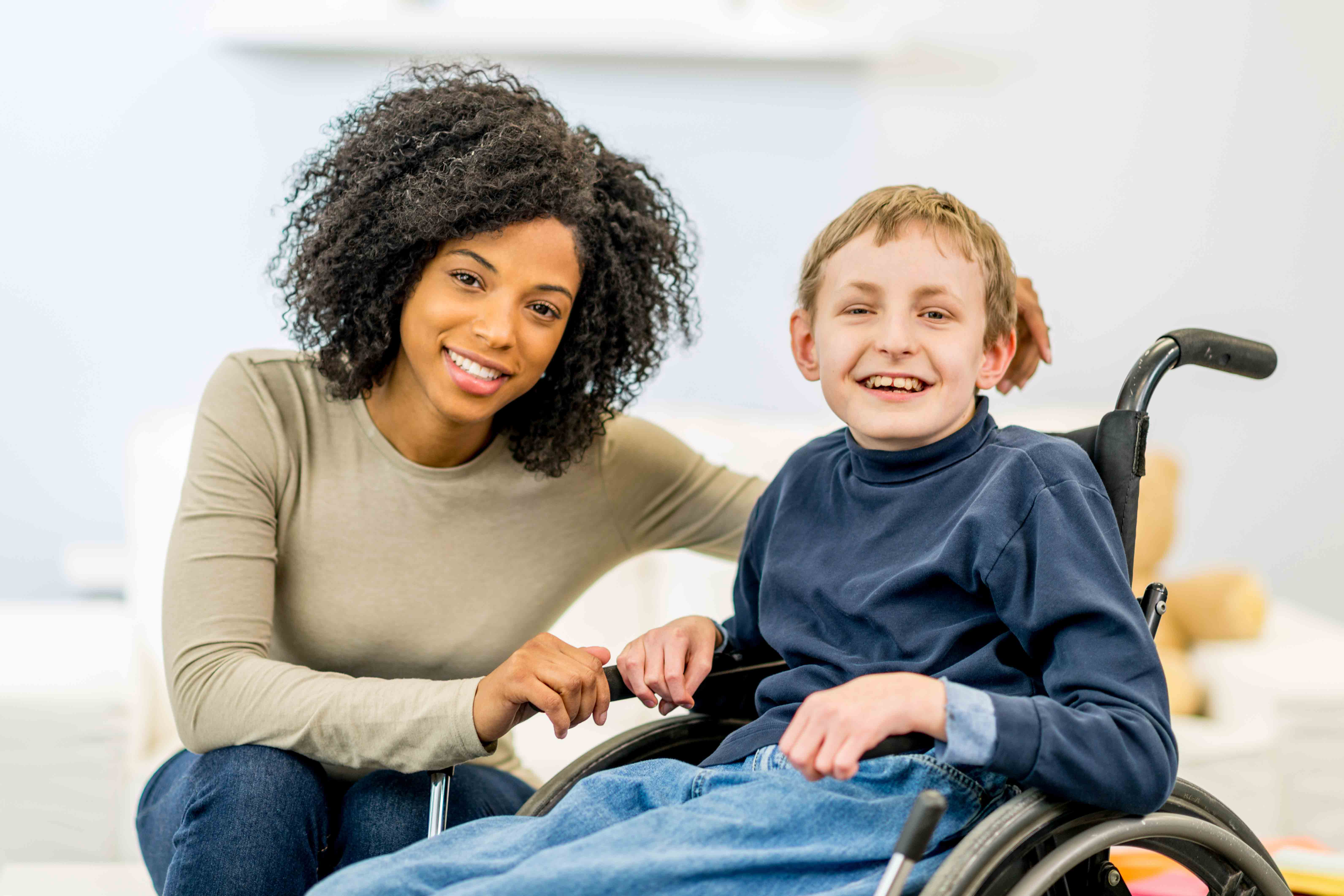 A caregiver sitting next to a smiling child in a wheelchair 