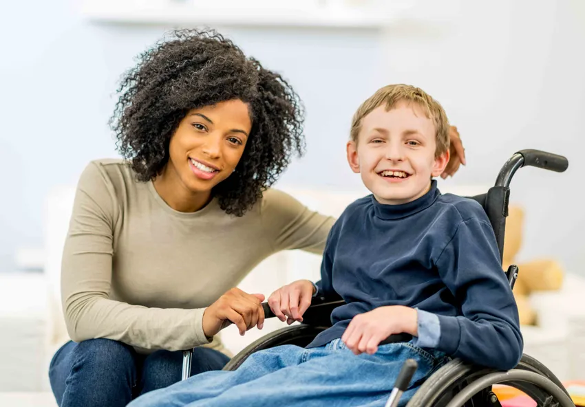 A caregiver sitting next to a smiling child in a wheelchair