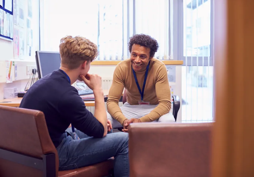 Man with curly hair leaning over desk to give another man advice