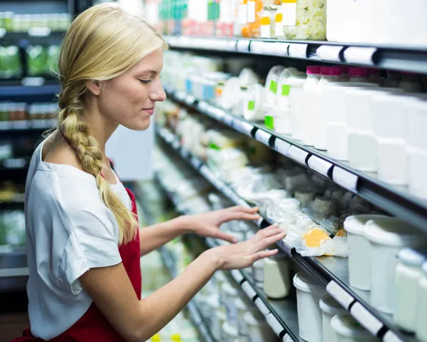 A person in an apron inspecting the dairy section at the store