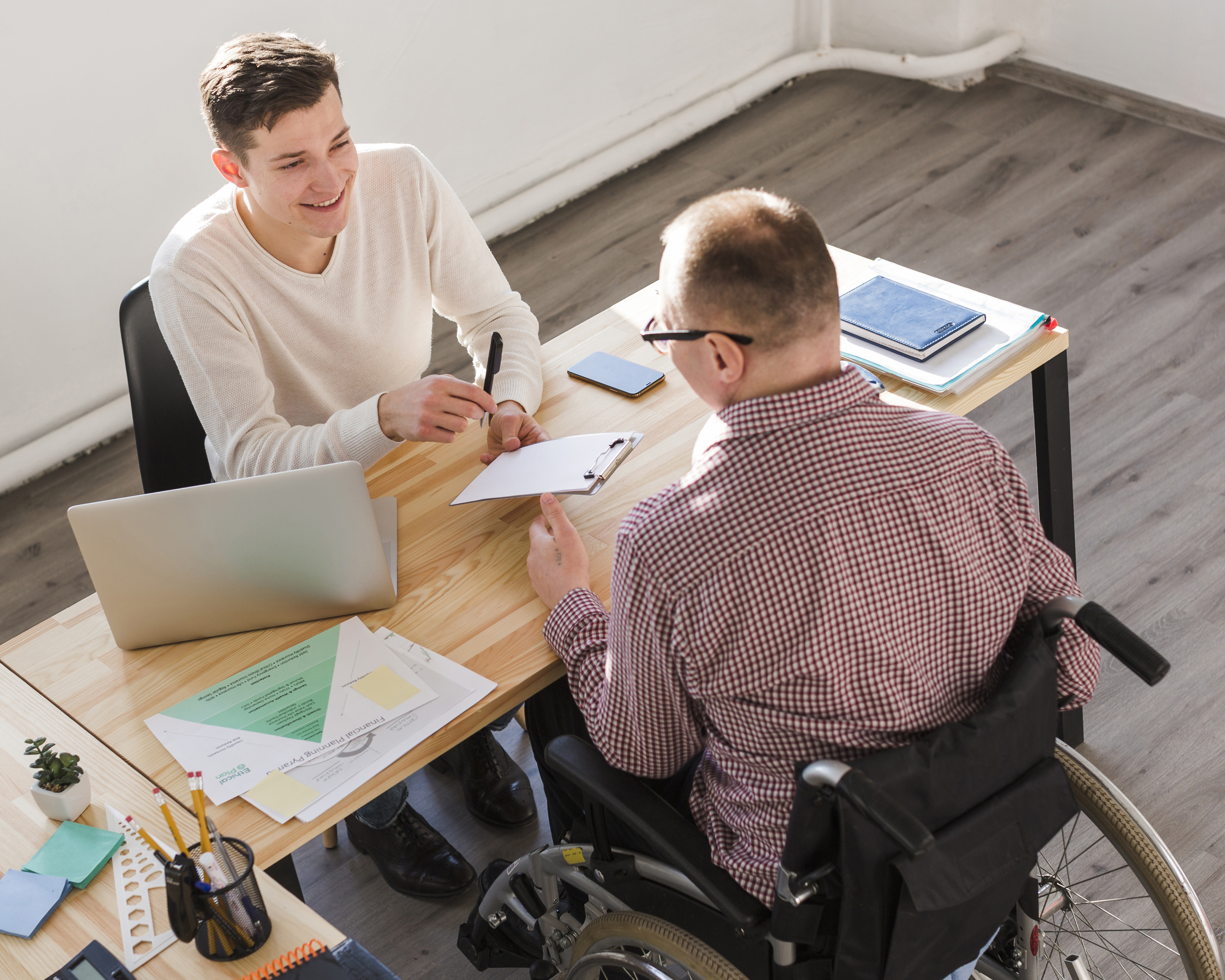 A man in a wheelchair sitting across a man extending a clipboard to him