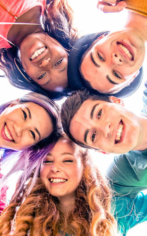 A group of kids in a huddle looking down at the camera smiling