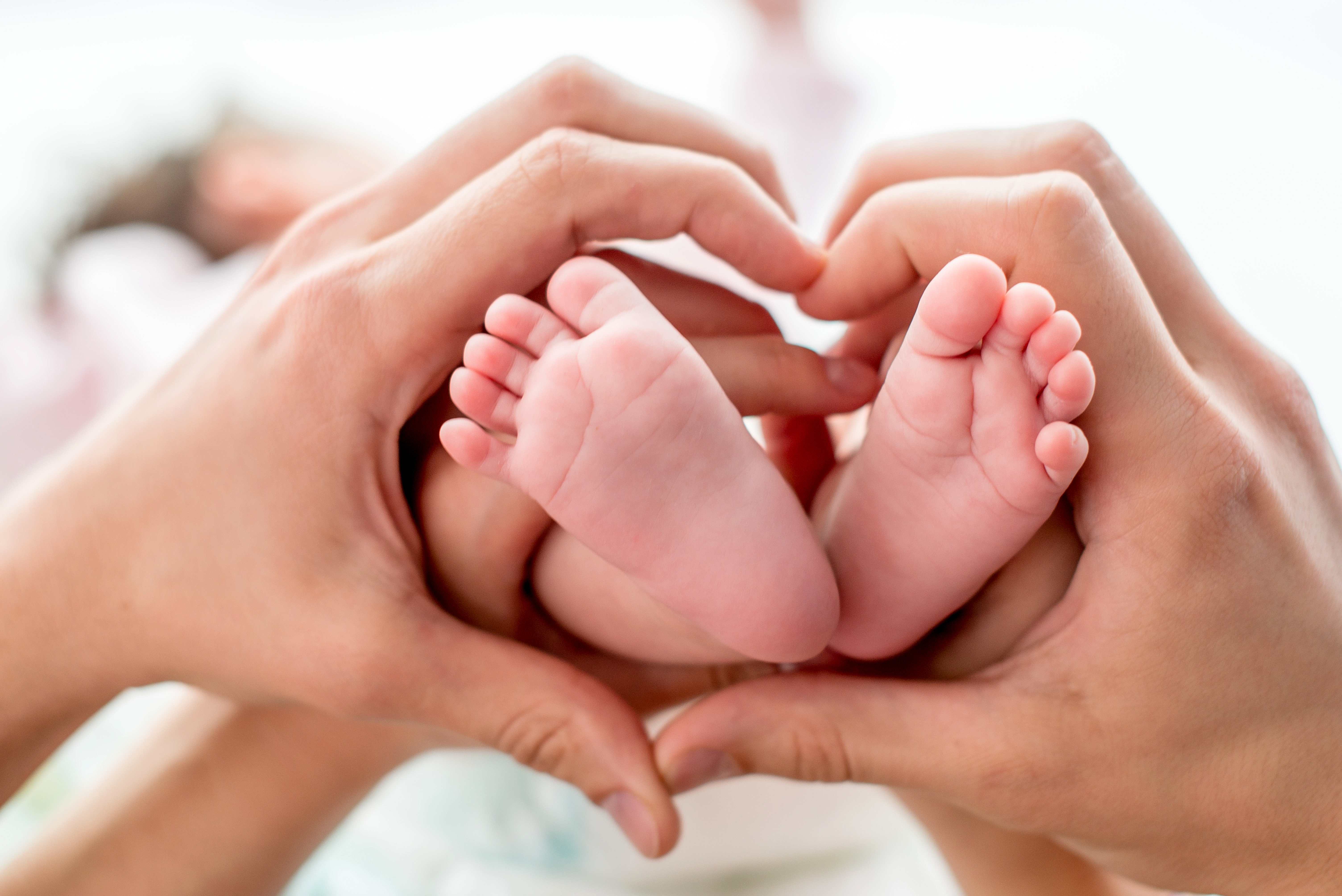Two hands positioned in a heart shape around a baby's feet