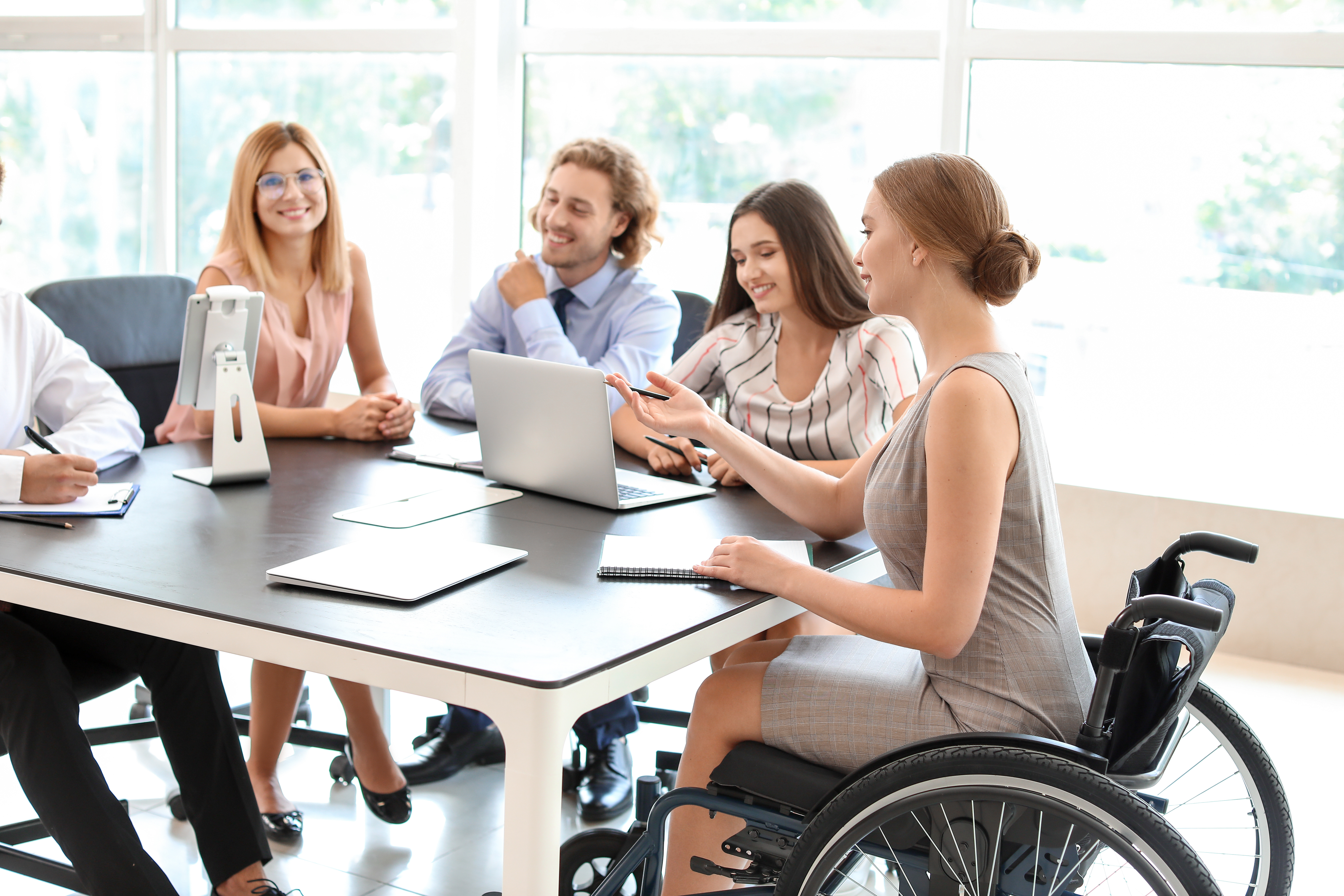 A group of employees around a table including a woman in a wheelchair leading the conversation