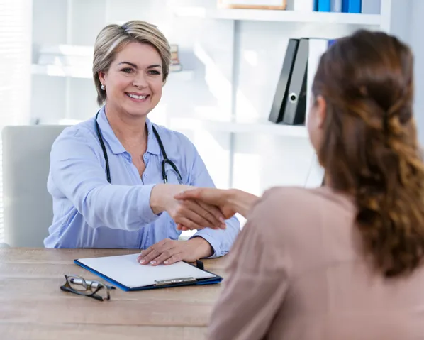 A doctor extending a hand to a patient and smiling