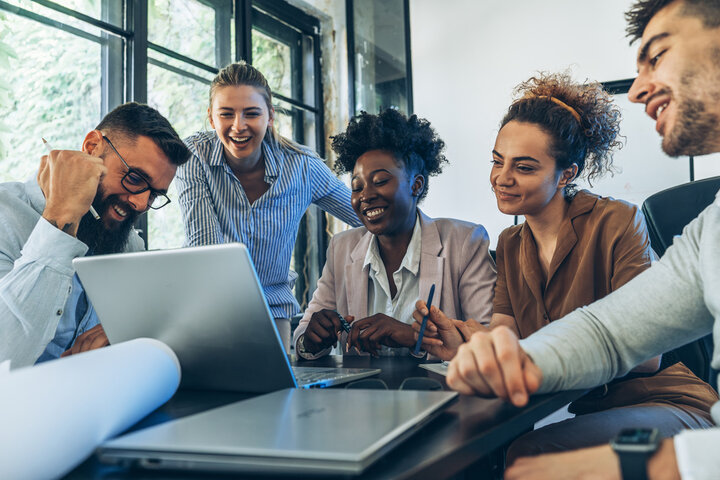 A group of interns around a laptop in a meeting smiling