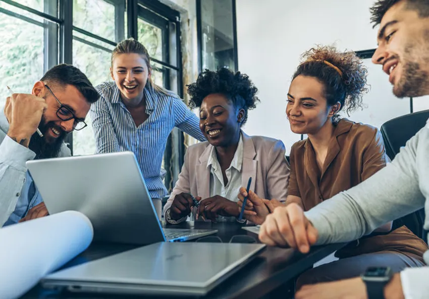 A group of interns around a laptop in a meeting smiling