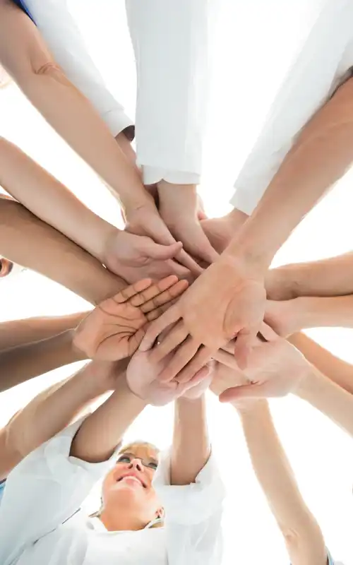 A group of people in light blue shirts extending their hands together