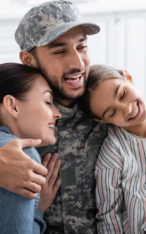 Man in camo holding his wife and daughter in a bear hug