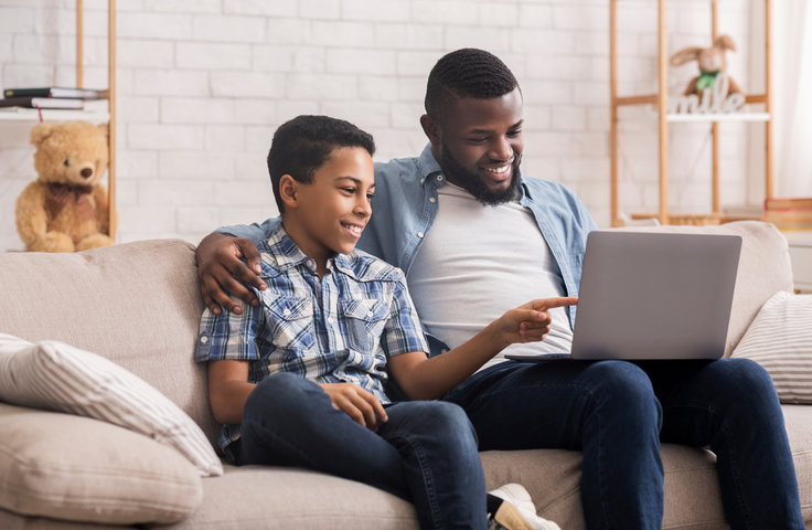 A son pointing to a laptop sitting next to his smiling father