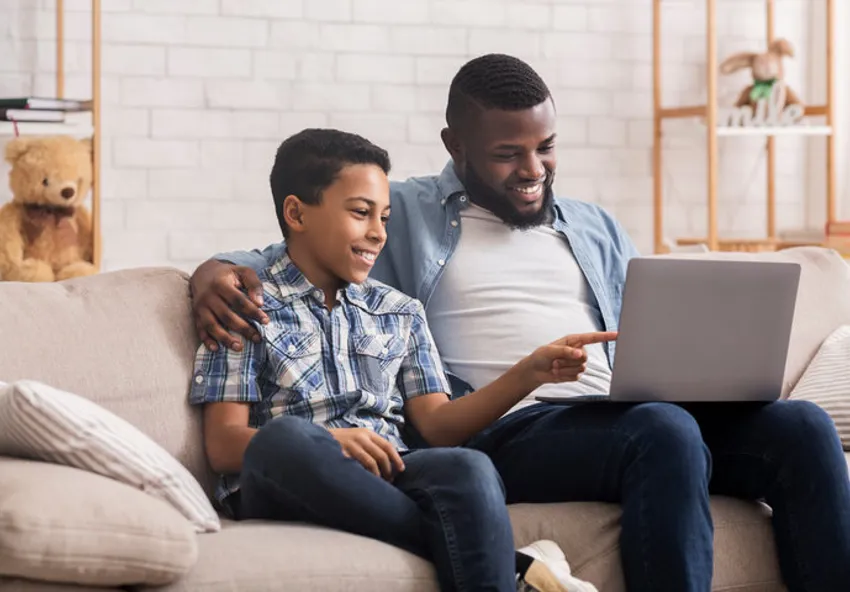 A son pointing to a laptop sitting next to his smiling father