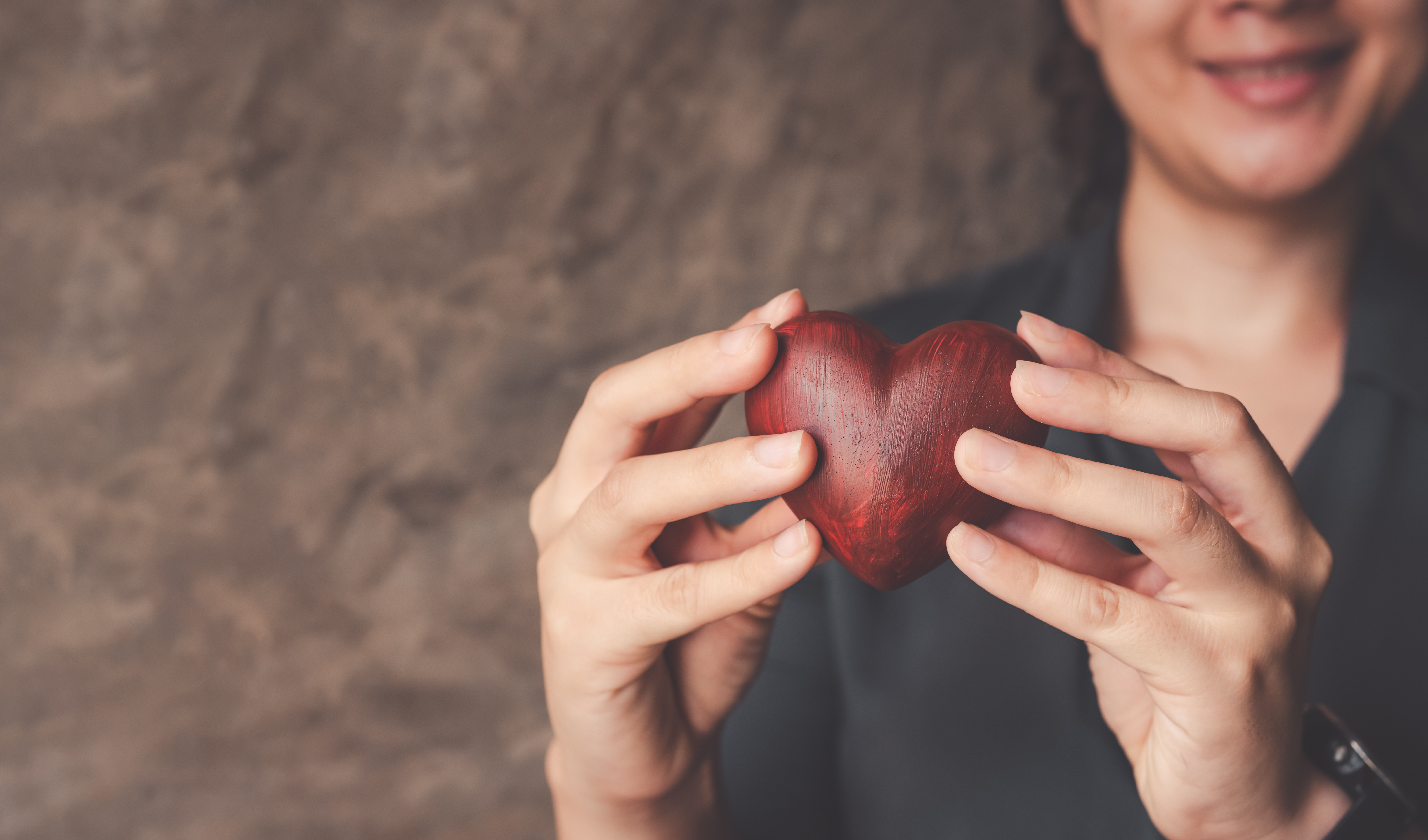 A person holding up a wooden heart to the camera