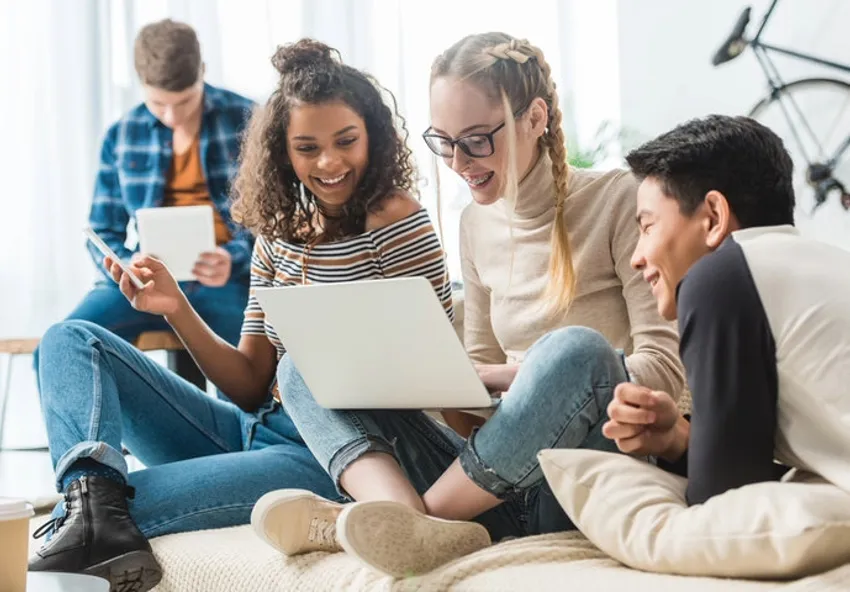 A group of teenagers sitting around a laptop smiling
