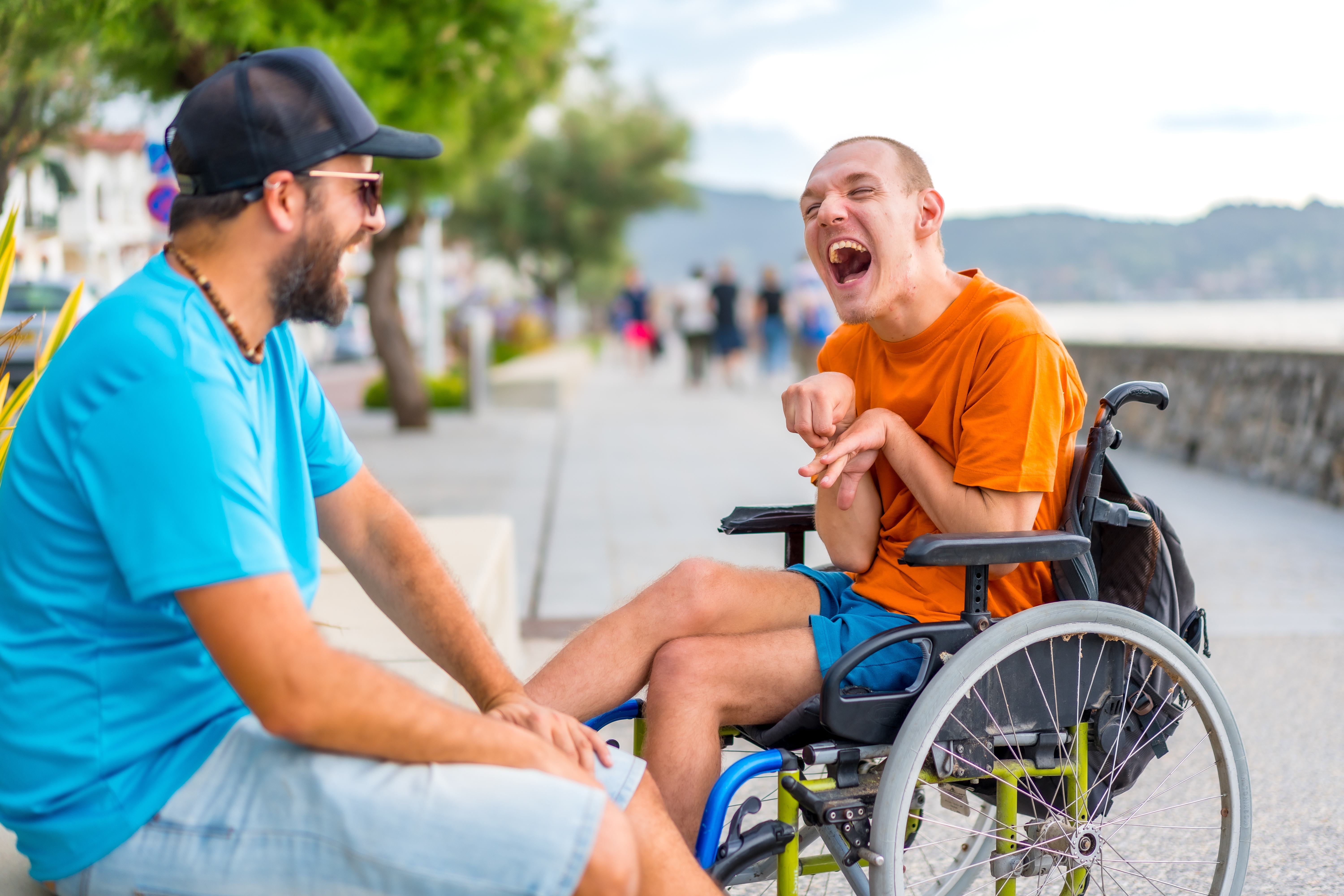 A man in a yellow wheelchair laughing with a man in a blue shirt at a park
