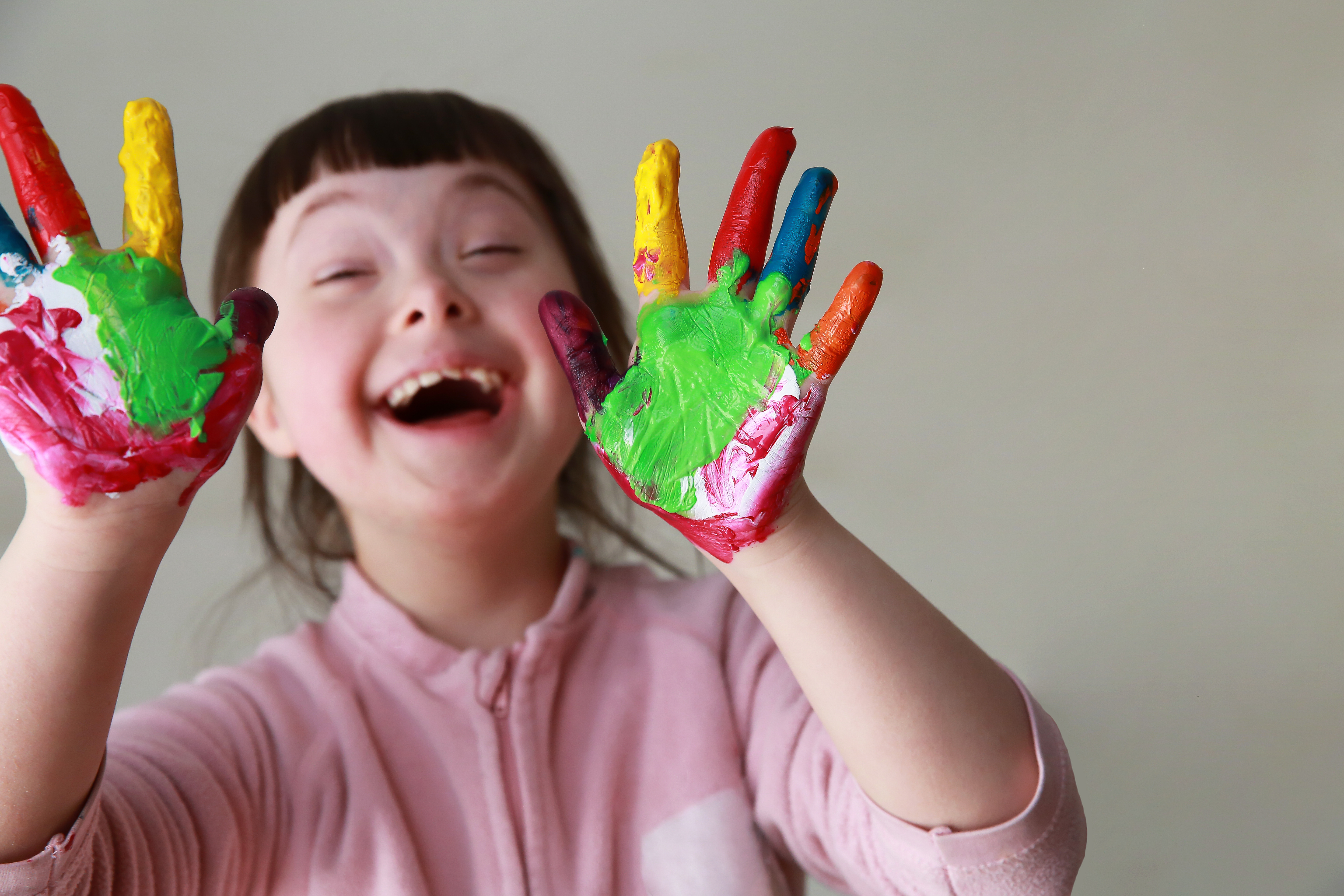 A child with paint messily on her hands smiling and laughing
