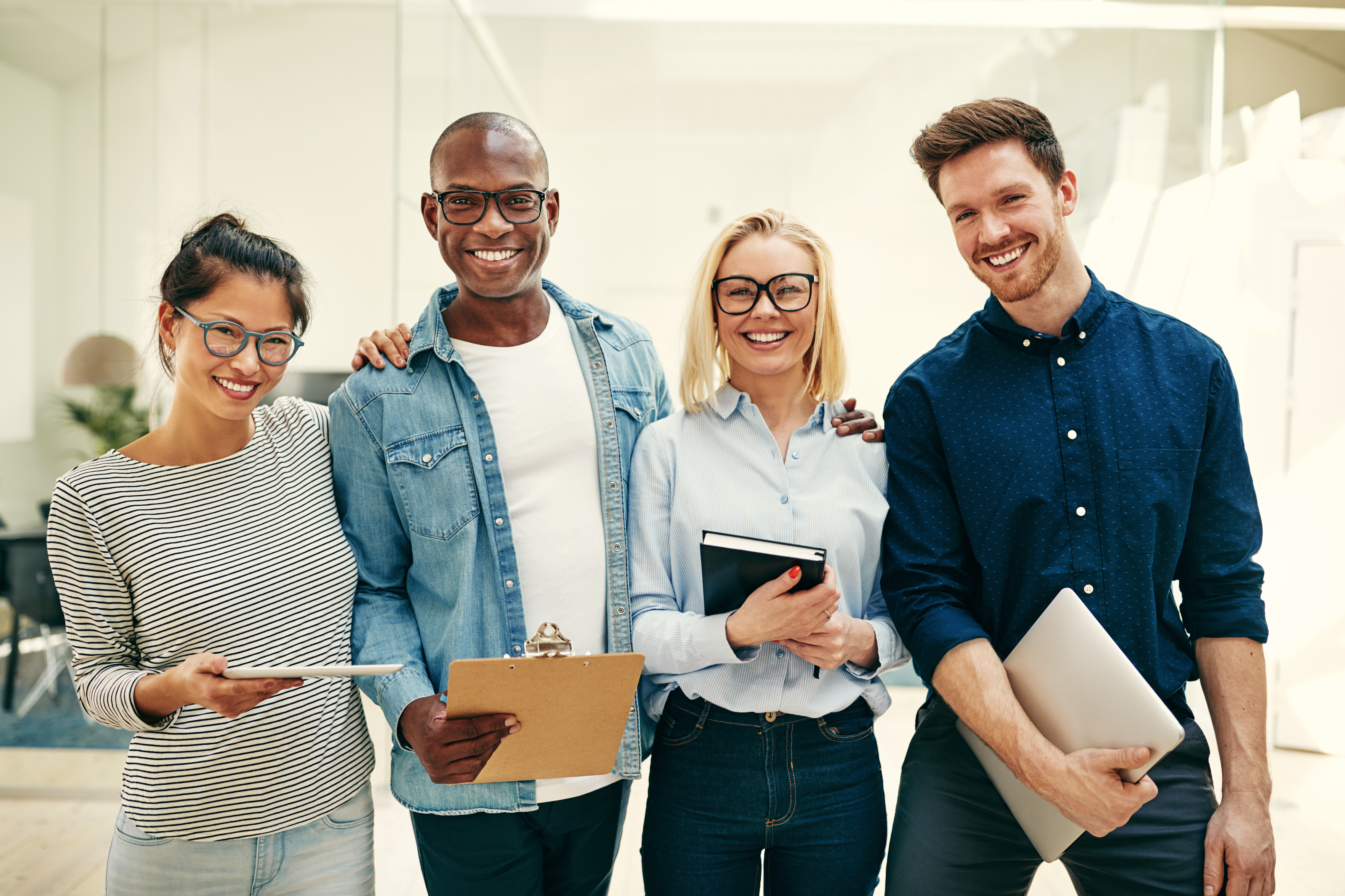 Group of diverse individuals smiling and holding clipboards and laptops