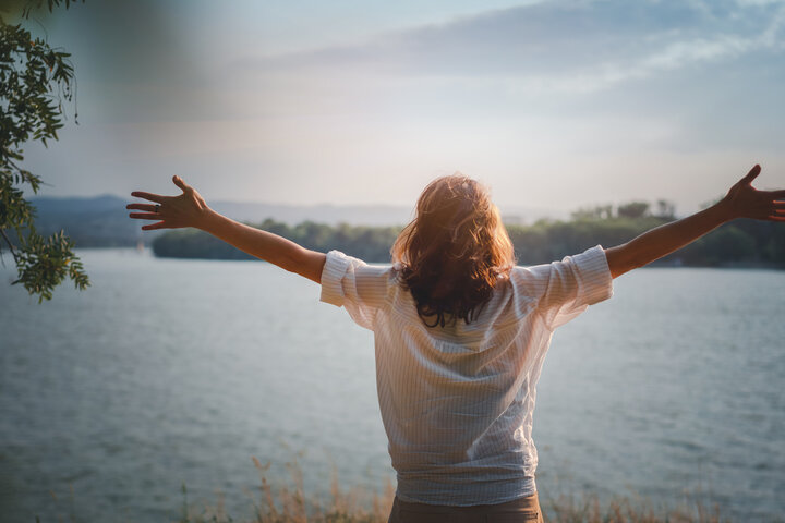 Woman with outstretched hands facing a lake